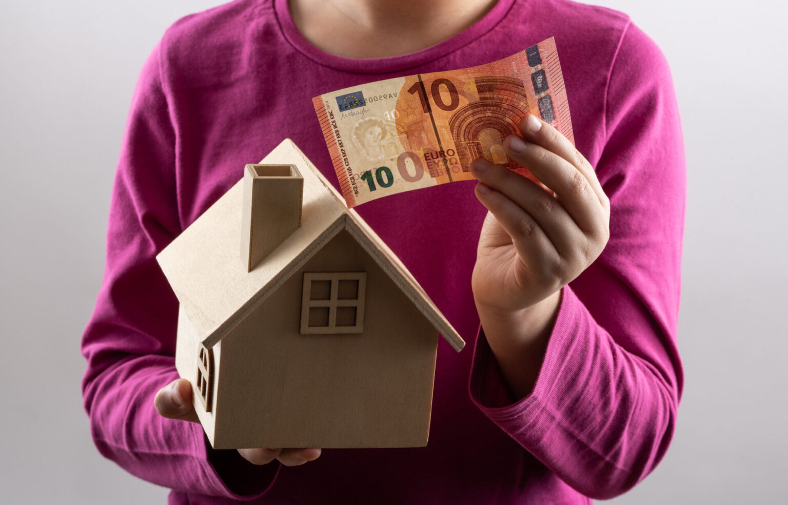 Miniature wooden house and 10 euro bill in children's hands